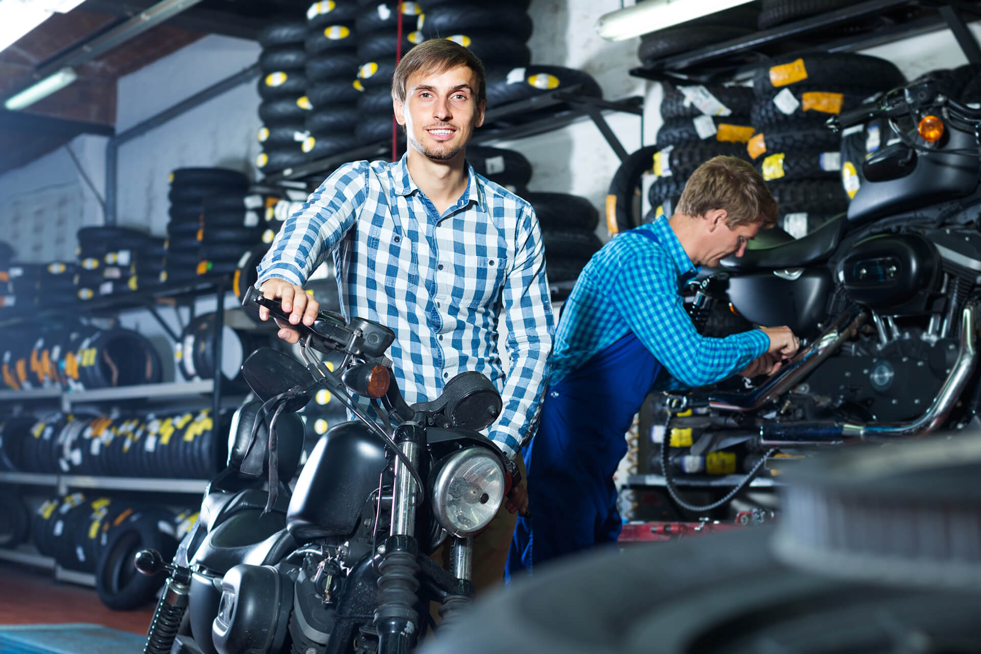 In einer Motoradwerkstatt schiebt ein Mitarbeiter ein Krad zum Arbeitsplatz